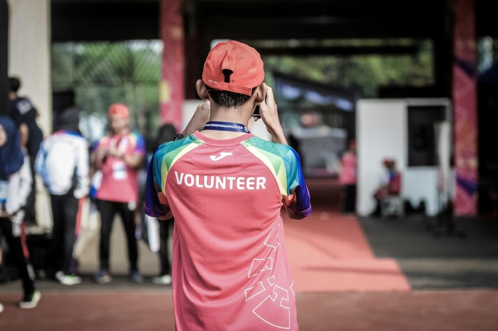 A man in a red shirt is holding a cell phone while engaging in philanthropy.