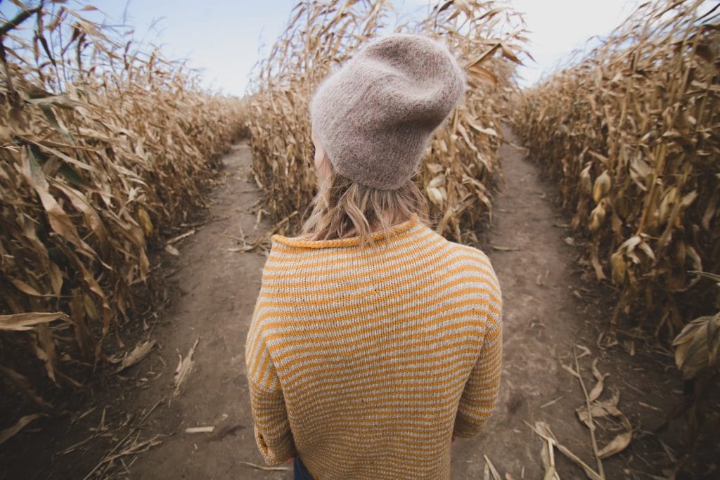 A woman, wearing a hat, navigating through a corn field with determination as she contemplates her decision about retiring early.