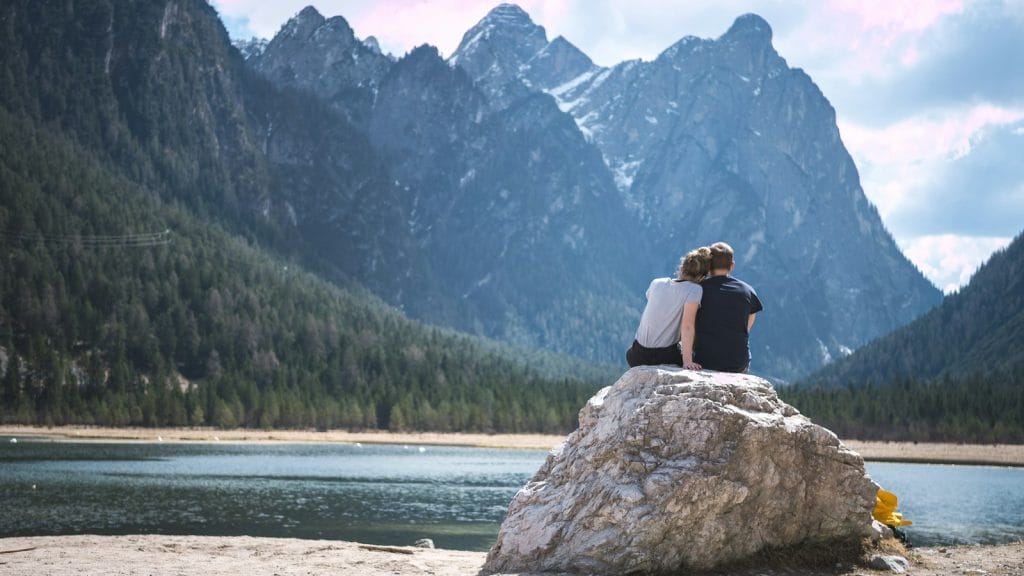 An early retirement couple sitting on a rock overlooking a lake.