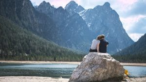 An early retirement couple sitting on a rock overlooking a lake.