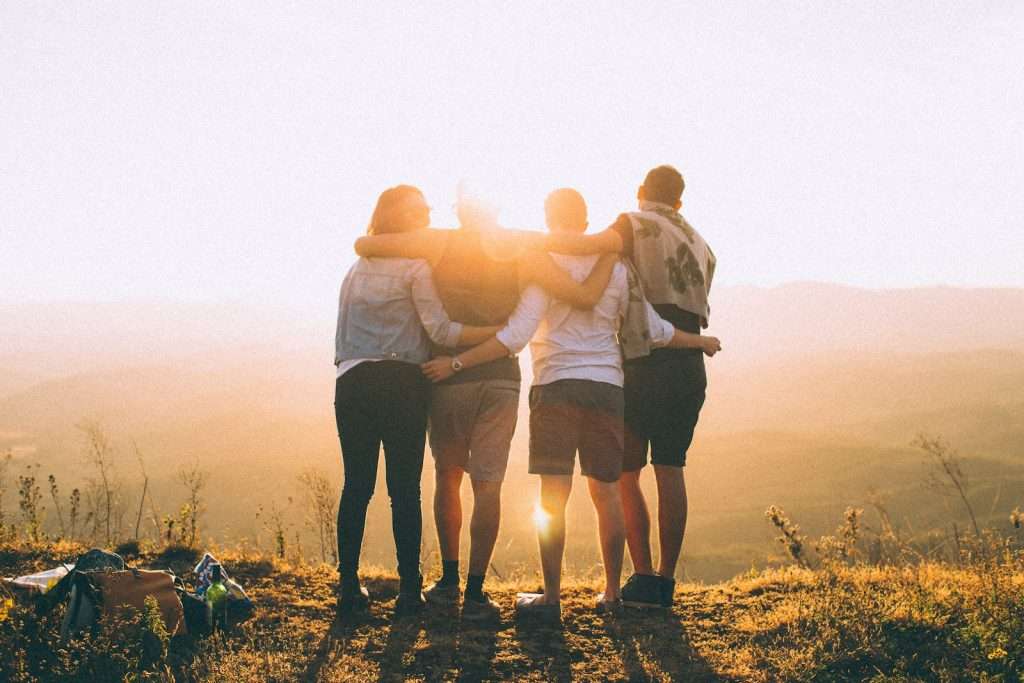 A group of friends enjoying early retirement standing on top of a mountain at sunset.