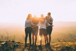 A group of friends enjoying early retirement standing on top of a mountain at sunset.